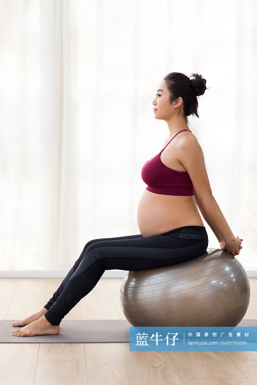 年轻孕妇坐在瑜伽球上