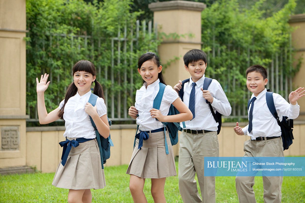 Cute Chinese schoolchildren in uniform waving at school yard