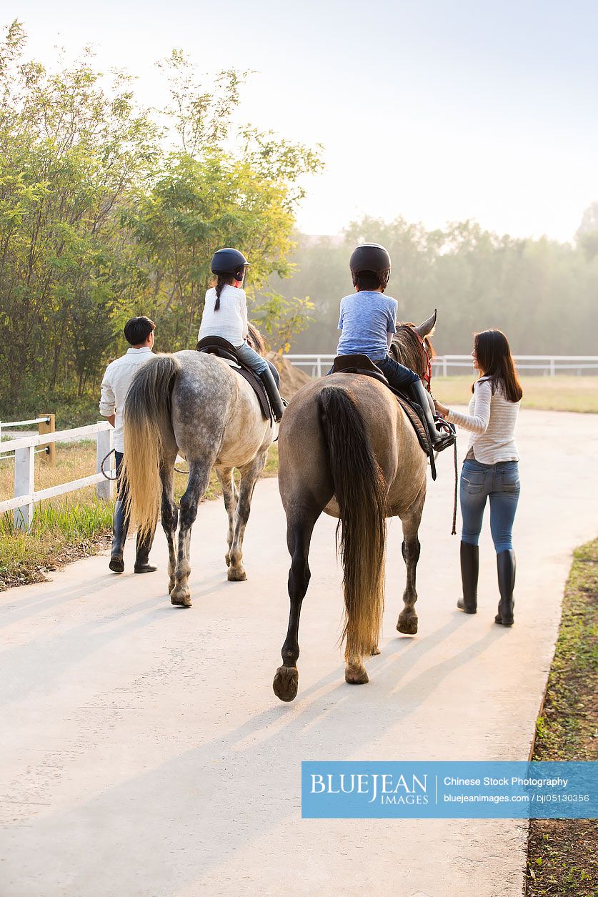 Cheerful young Chinese family riding horses