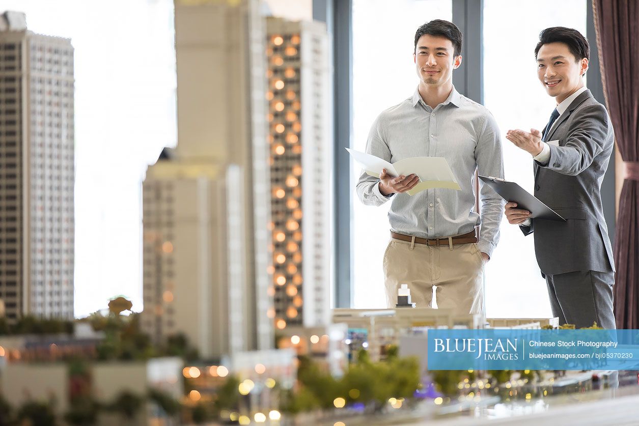 Chinese realtor showing architectural model to young man