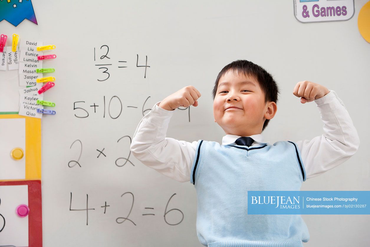 A young Chinese student flexing his muscles in front of a whiteboard