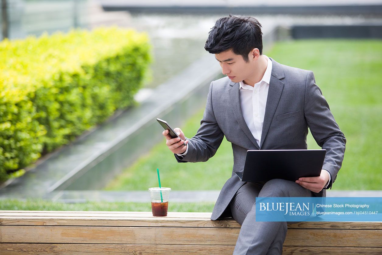 Young Chinese businessman working with laptop outdoors