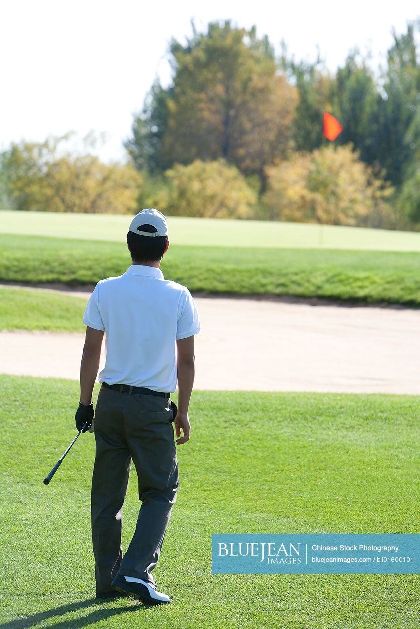 Young Chinese man watching golf ball