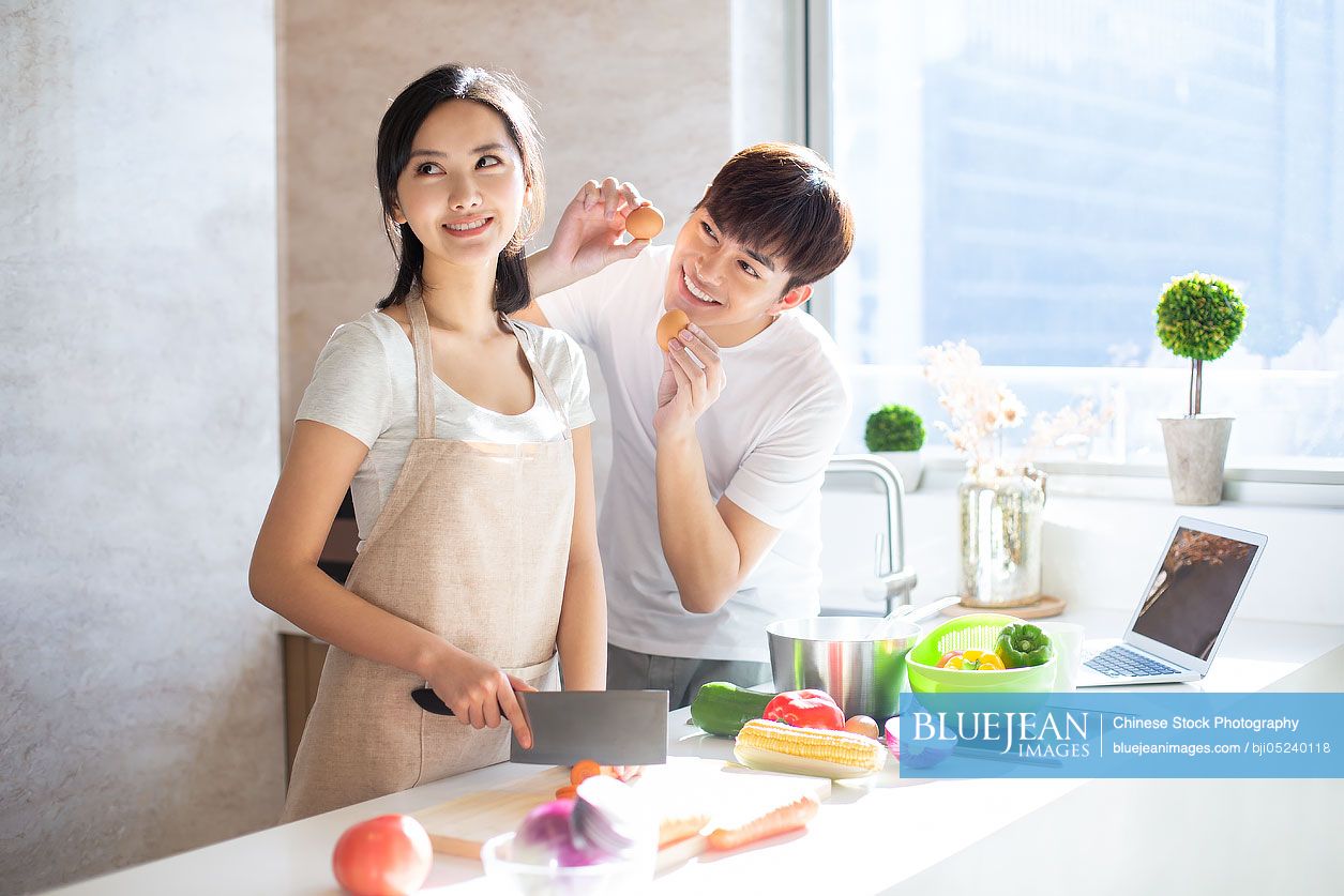 Happy young Chinese couple cooking in kitchen