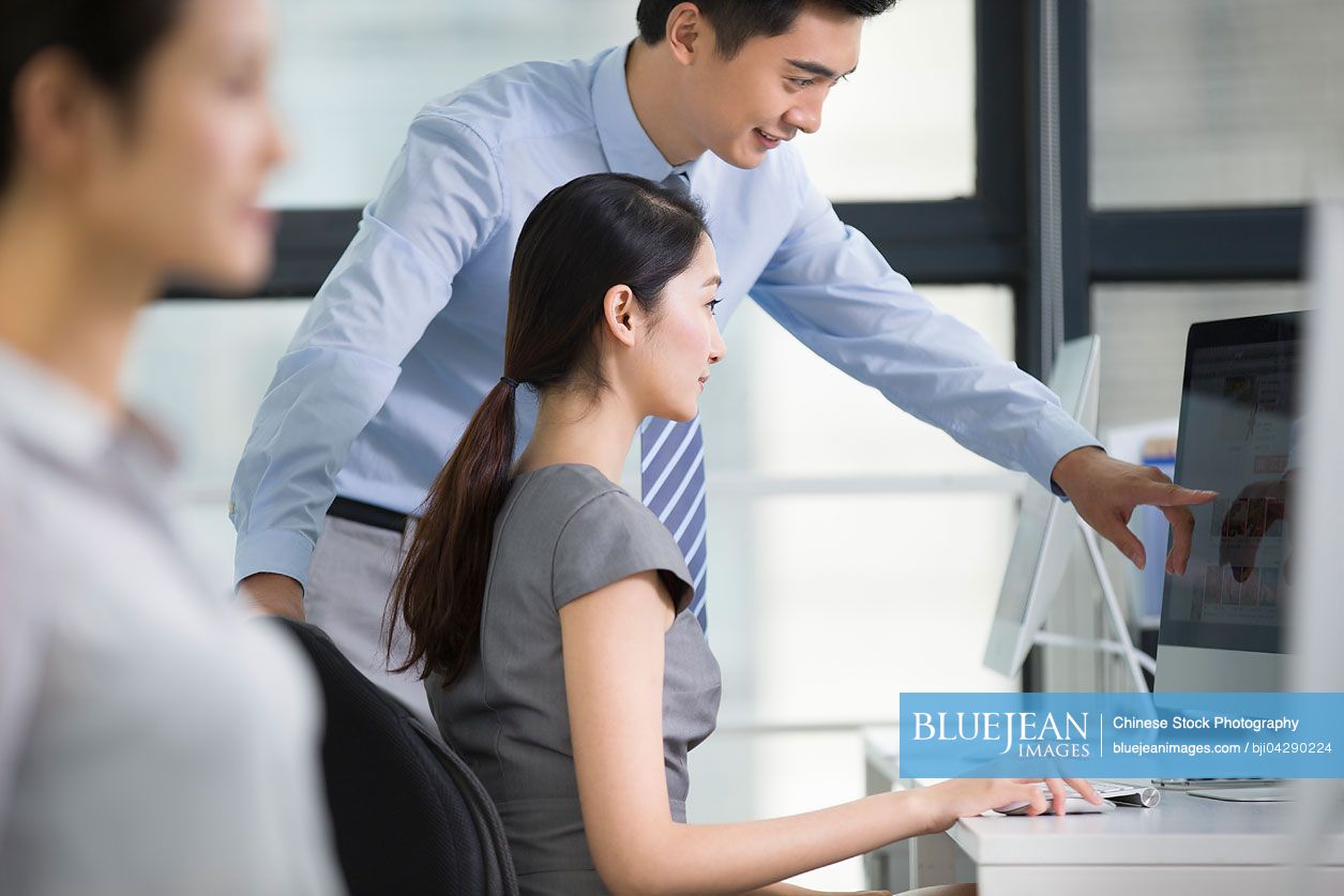 Young Chinese businesswoman and businessman talking in office