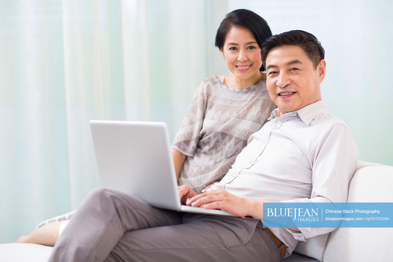 Happy mature Chinese couple with laptop at home
