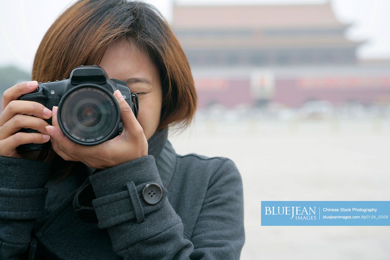 Young Chinese woman taking a photo in front of Tiananmen Square, Beijing, China