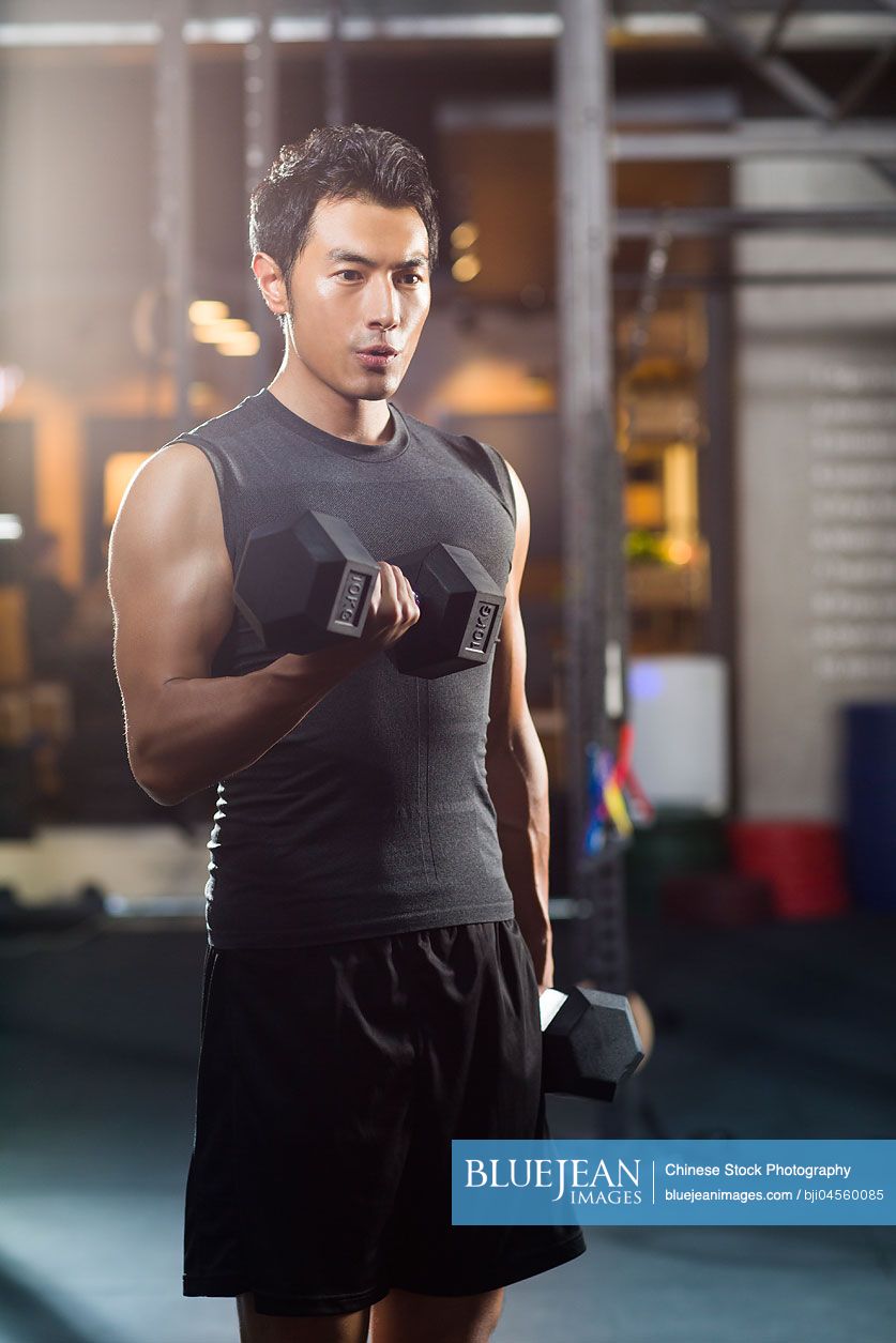 Young Chinese man lifting weights at gym