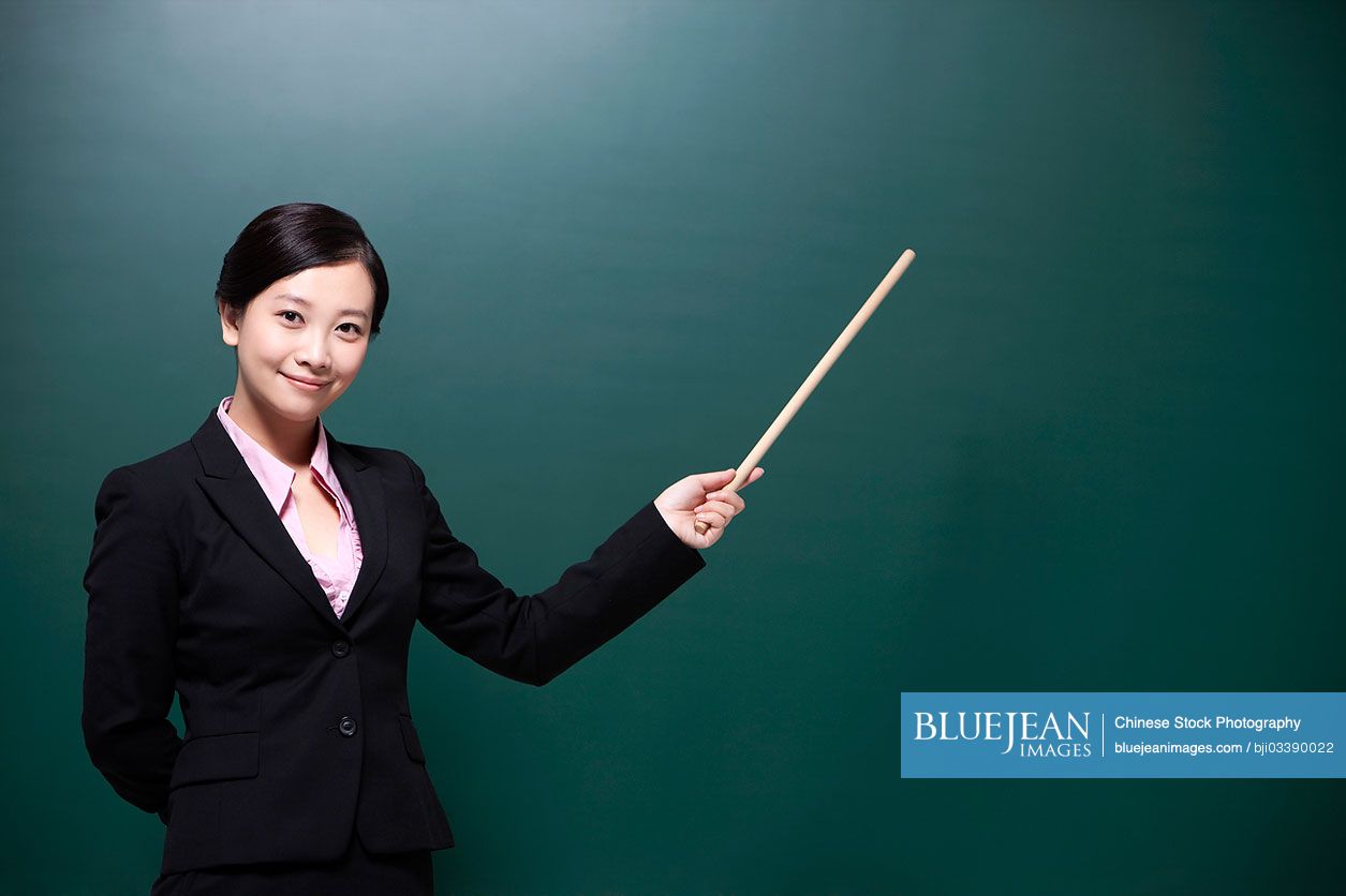 Happy female Chinese teacher holding Chinese teacher's pointer in classroom