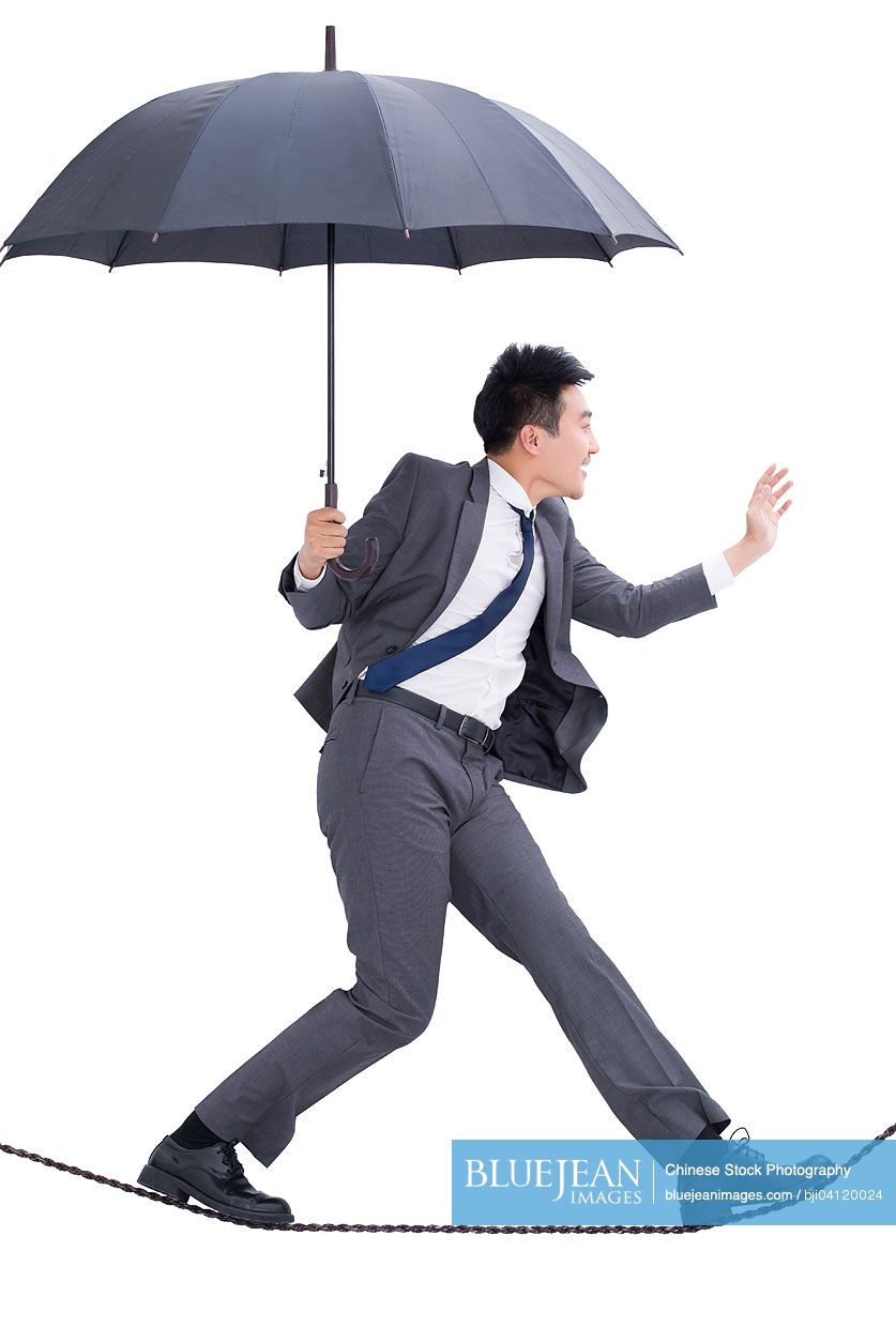 Chinese business man walking on rope with umbrella