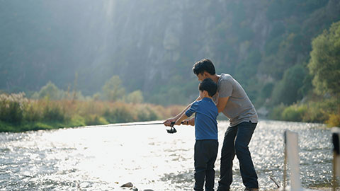 Cheerful Chinese father teaching son fishing