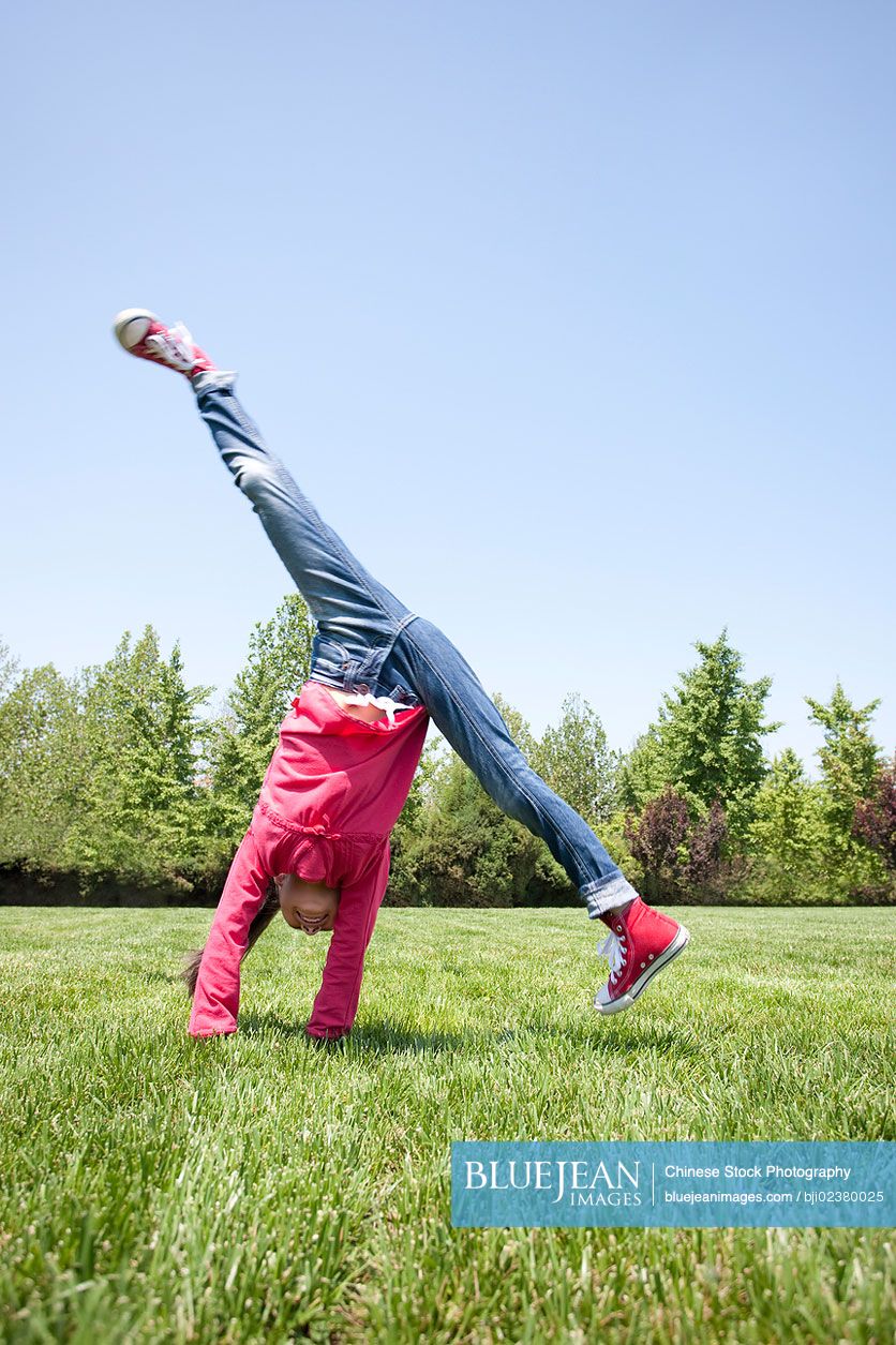 Young Chinese girl doing cartwheel in field