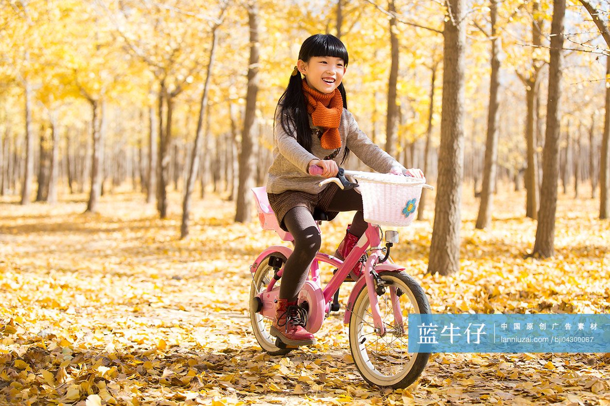 小女孩在秋日的树林里骑自行车