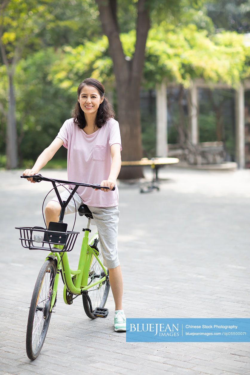 Happy mature Chinese woman riding bike in park