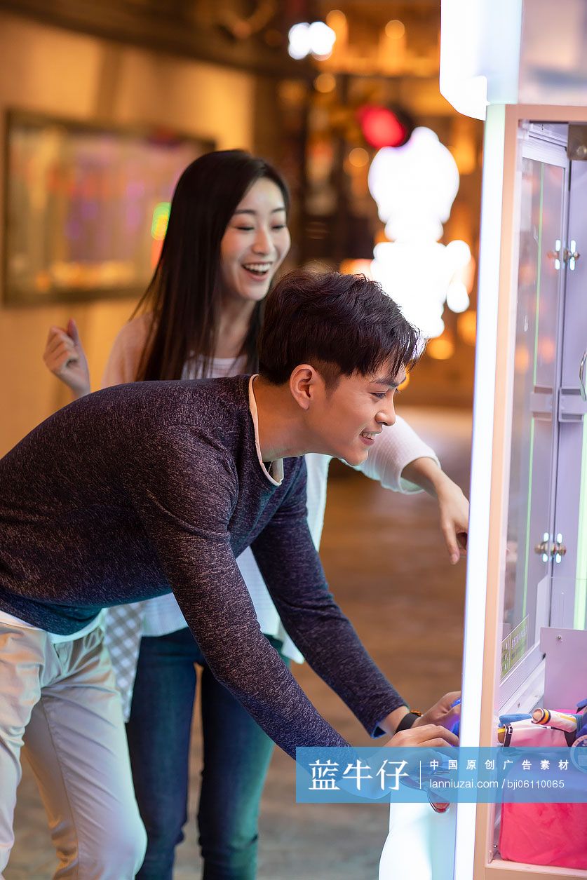 快乐的年轻情侣在商场玩抓娃娃机游戏