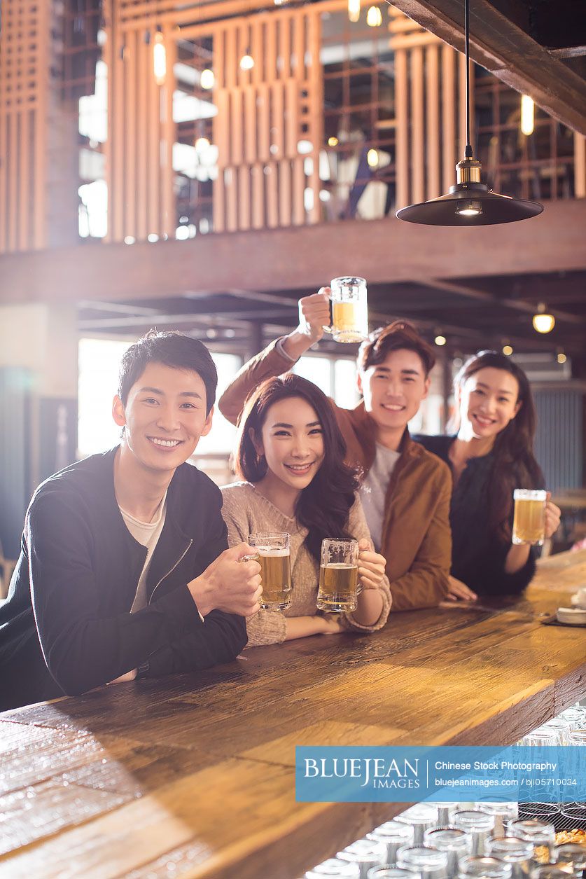 Happy Chinese friends drinking beer and toasting in bar