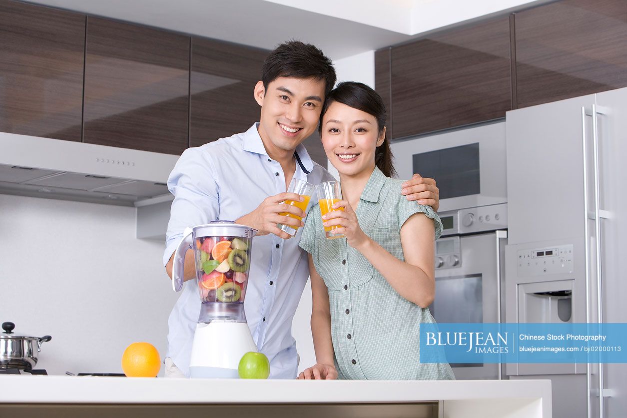 Young Chinese couple drinking fresh fruit juice in kitchenHighres