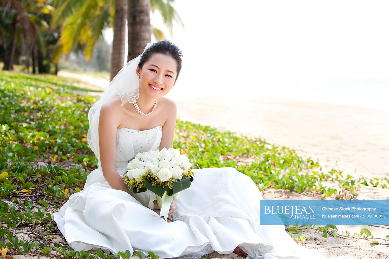 Happy Chinese bride sitting on the beach