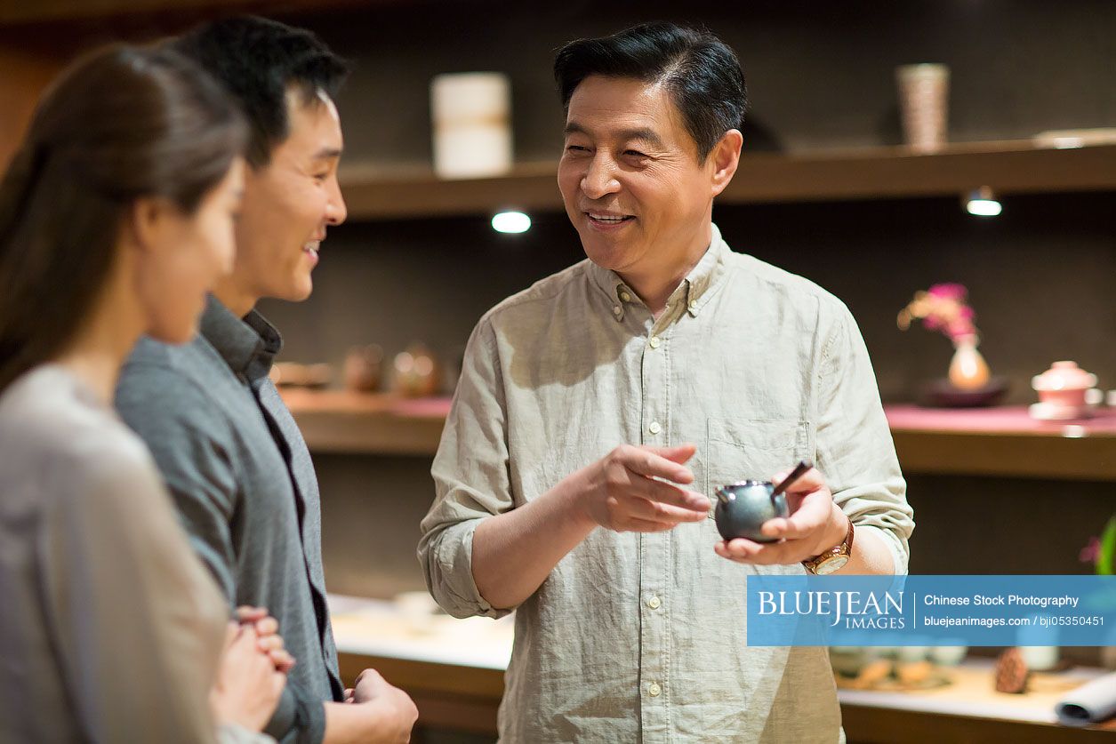 Mature Chinese man showing a teapot to customers