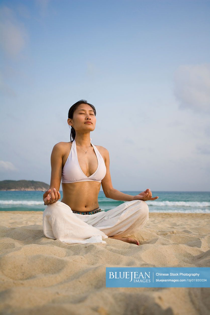 Young Chinese woman doing yoga on the beach