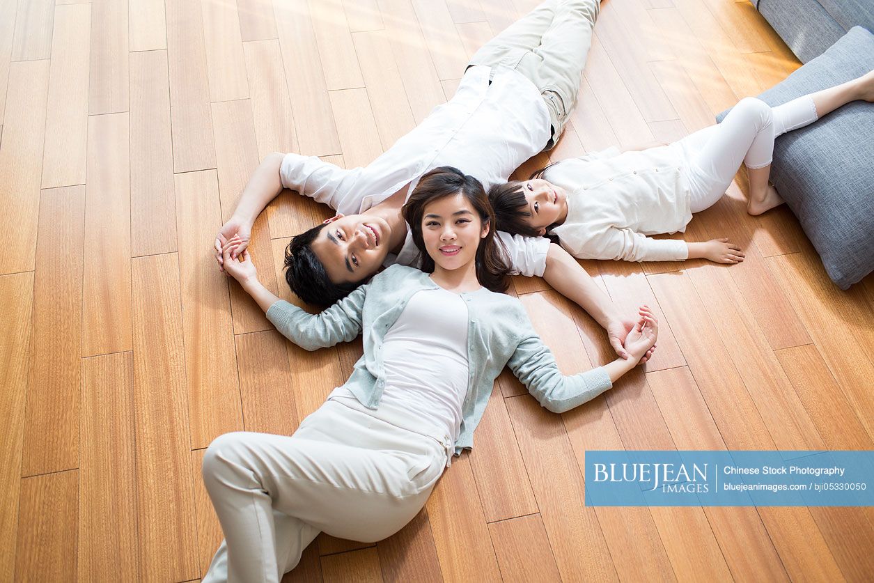 Happy young Chinese family resting on wooden floor