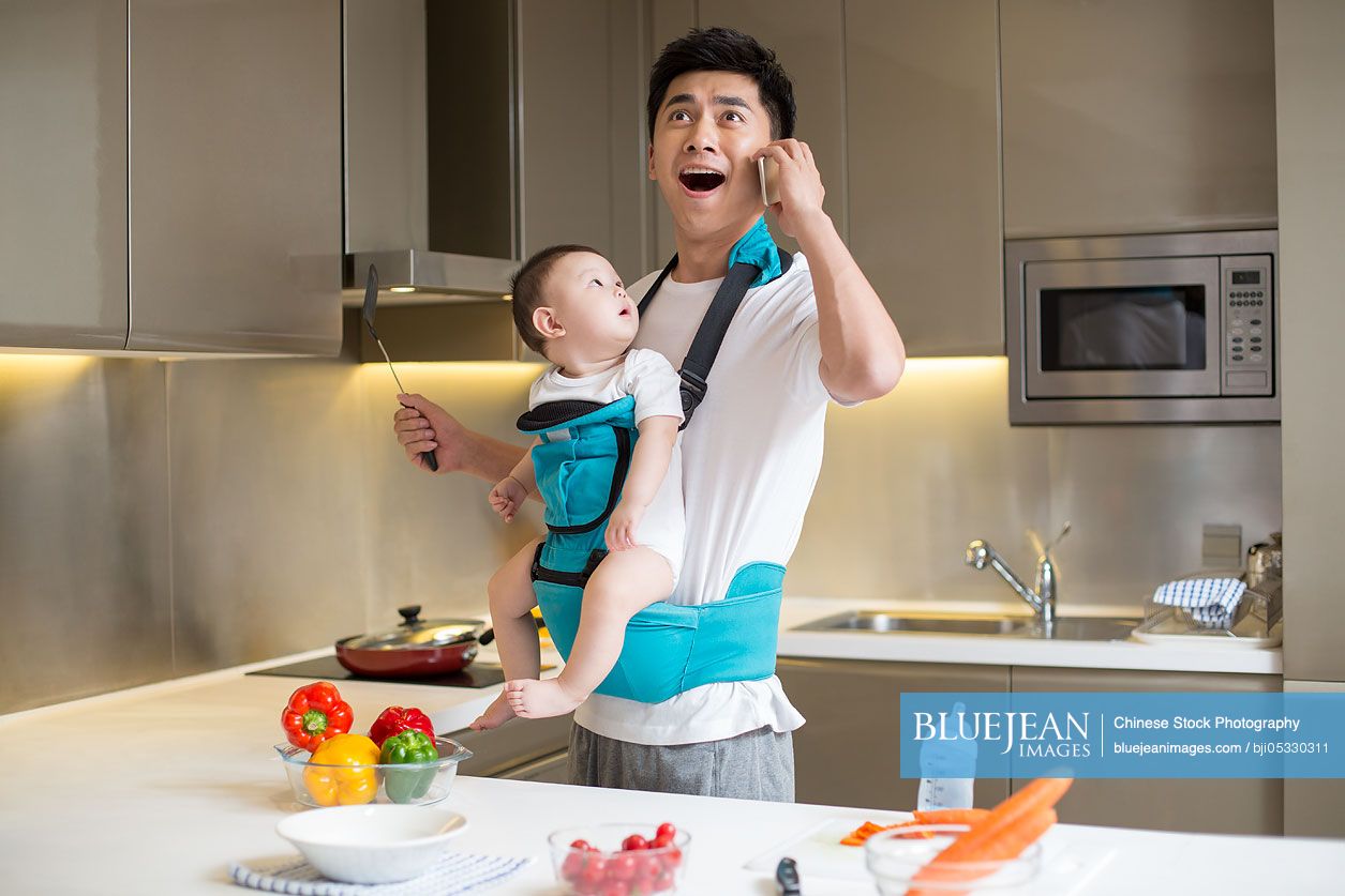 Chinese father holding baby and talking on the phone in kitchen