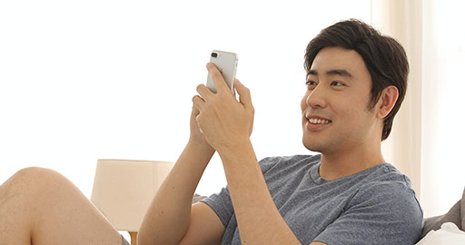 Happy young Chinese man playing mobile games in bedroom,4K