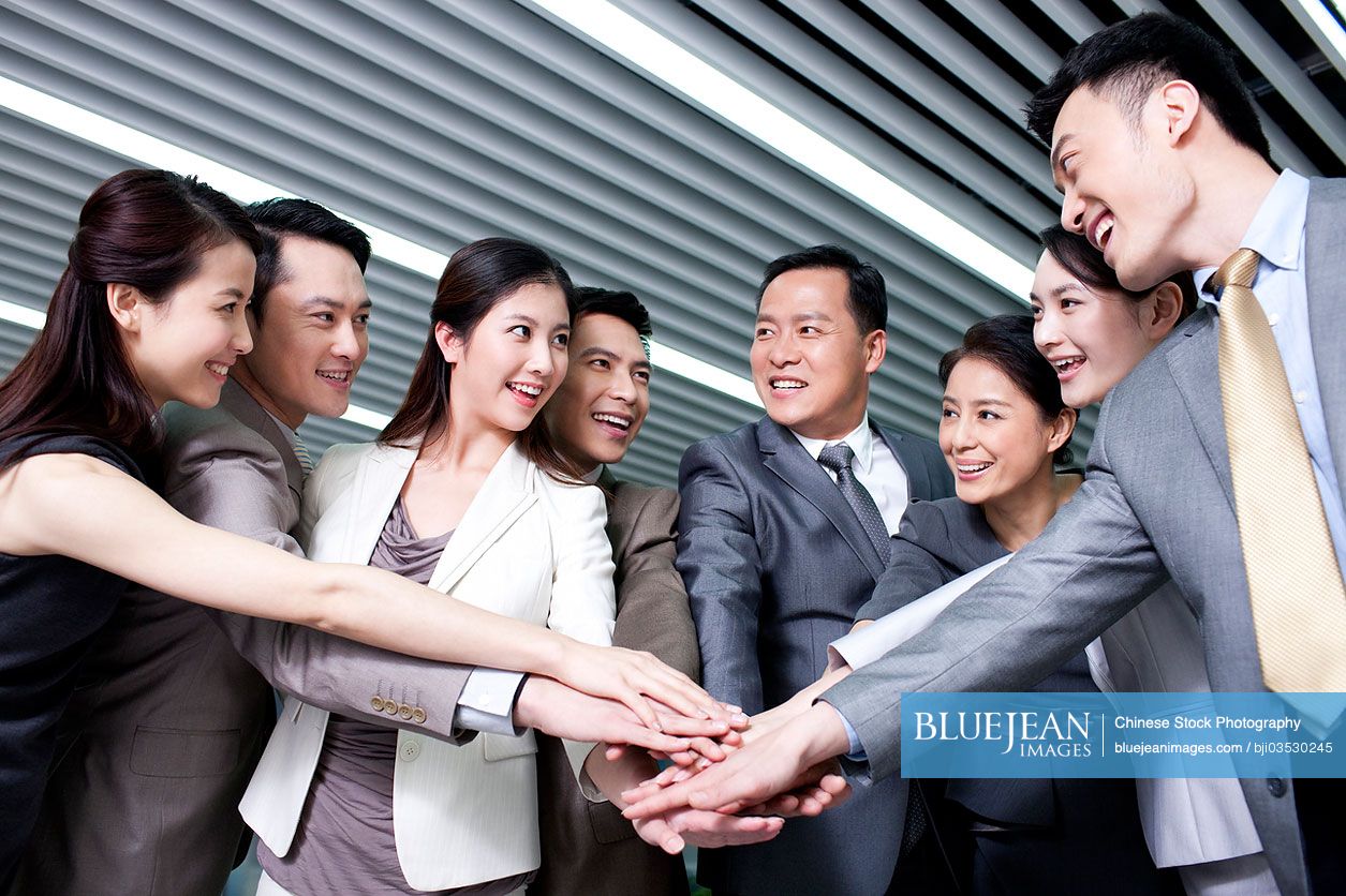 Cheerful Chinese businesspeople stacking hands
