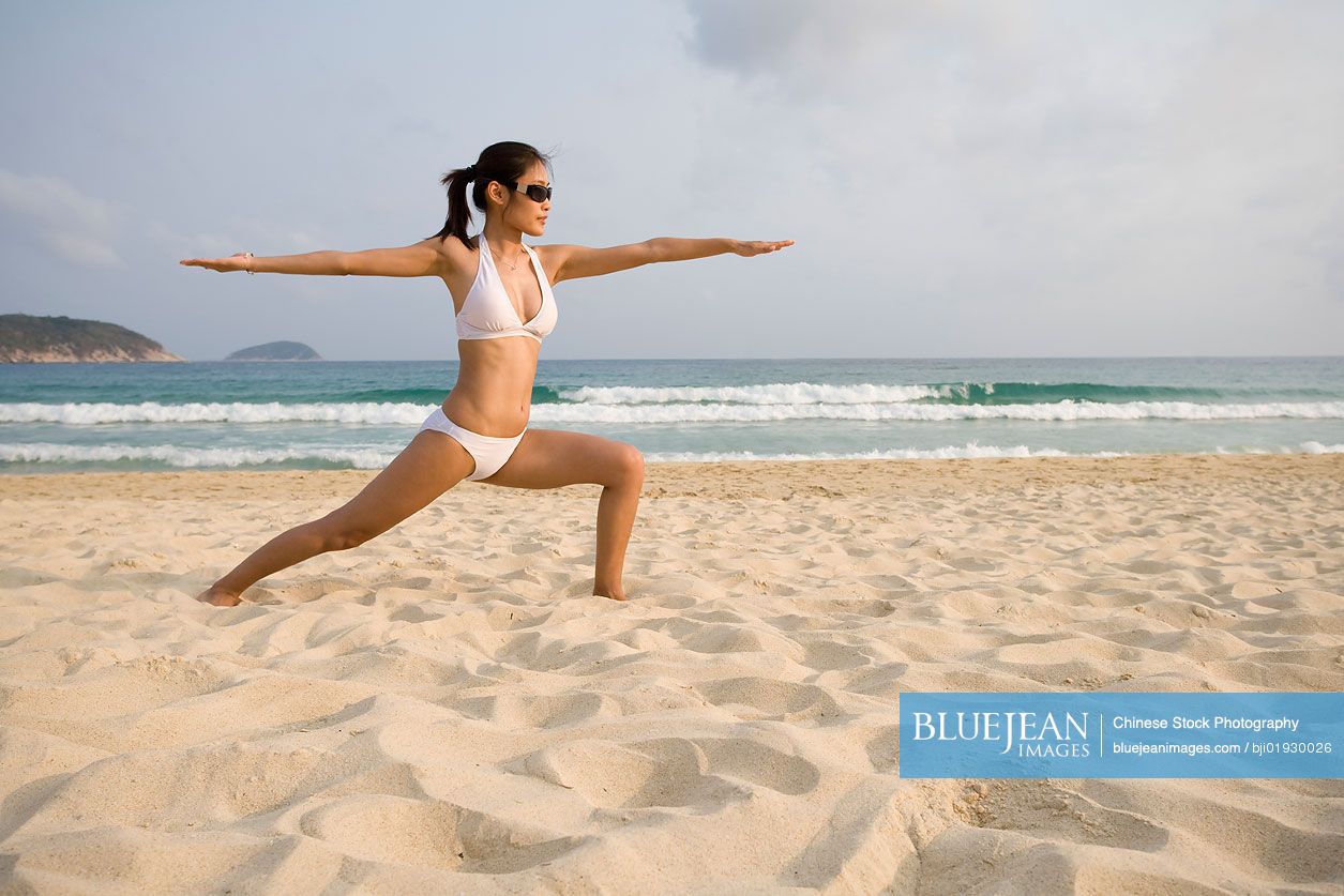 Young Chinese woman doing yoga on the beach