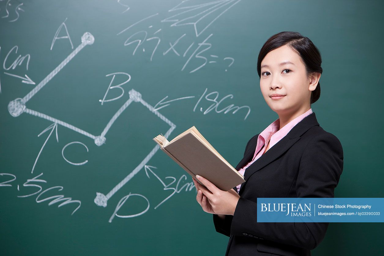 Serious female Chinese teacher holding textbooks in classroom