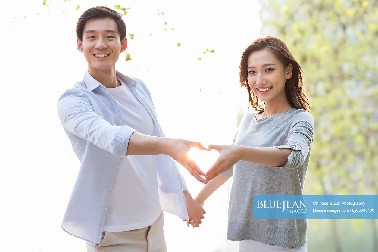 Happy young Chinese couple doing heart shape gesture