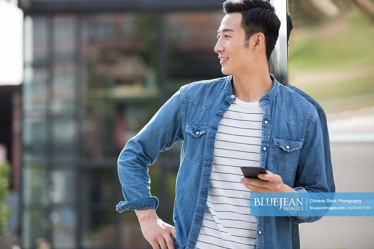 Cheerful young Chinese man holding a smart phone