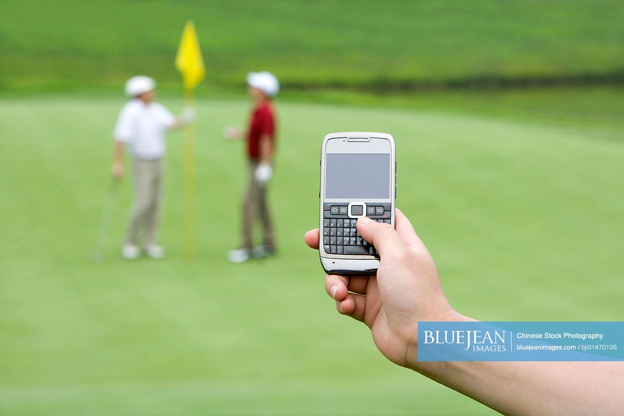 Close-up of a cellphone, two Chinese golfers in background