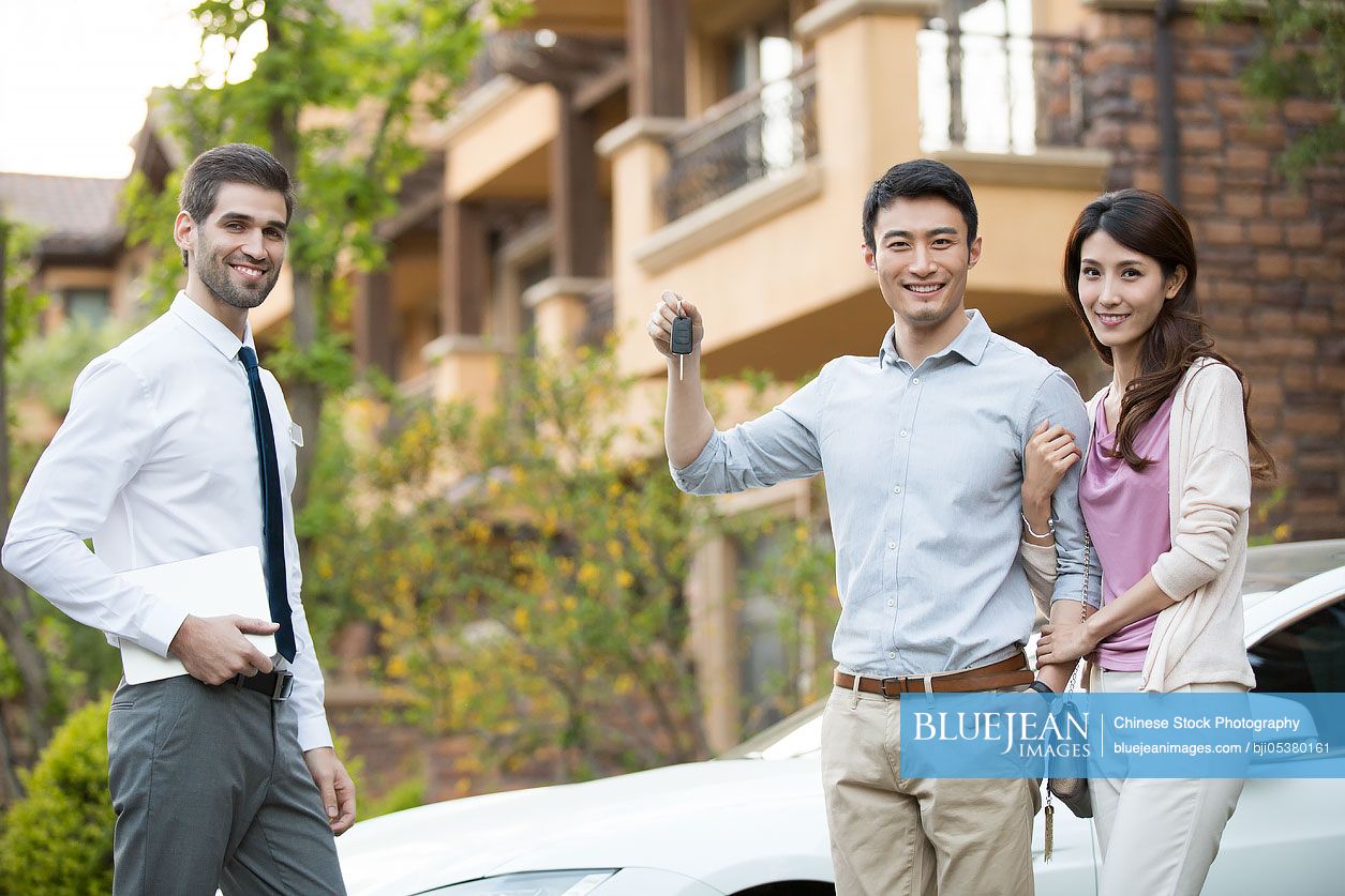 Happy young Chinese couple receiving car key from car salesperson