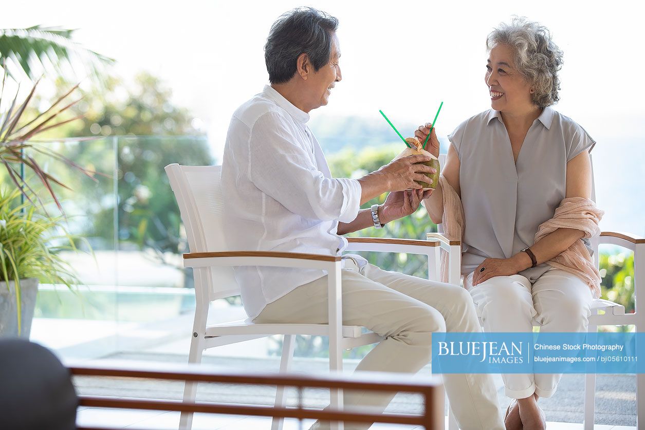 Happy senior Chinese couple drinking coconut milk on balcony
