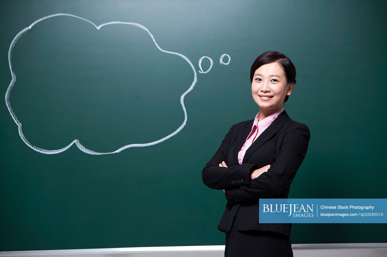 Cheerful female Chinese teacher arms crossed in classroom