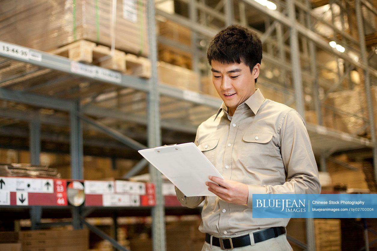 Male Chinese warehouse worker with clipboard