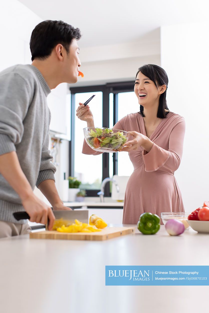 Happy Chinese pregnant woman and husband cooking in kitchen