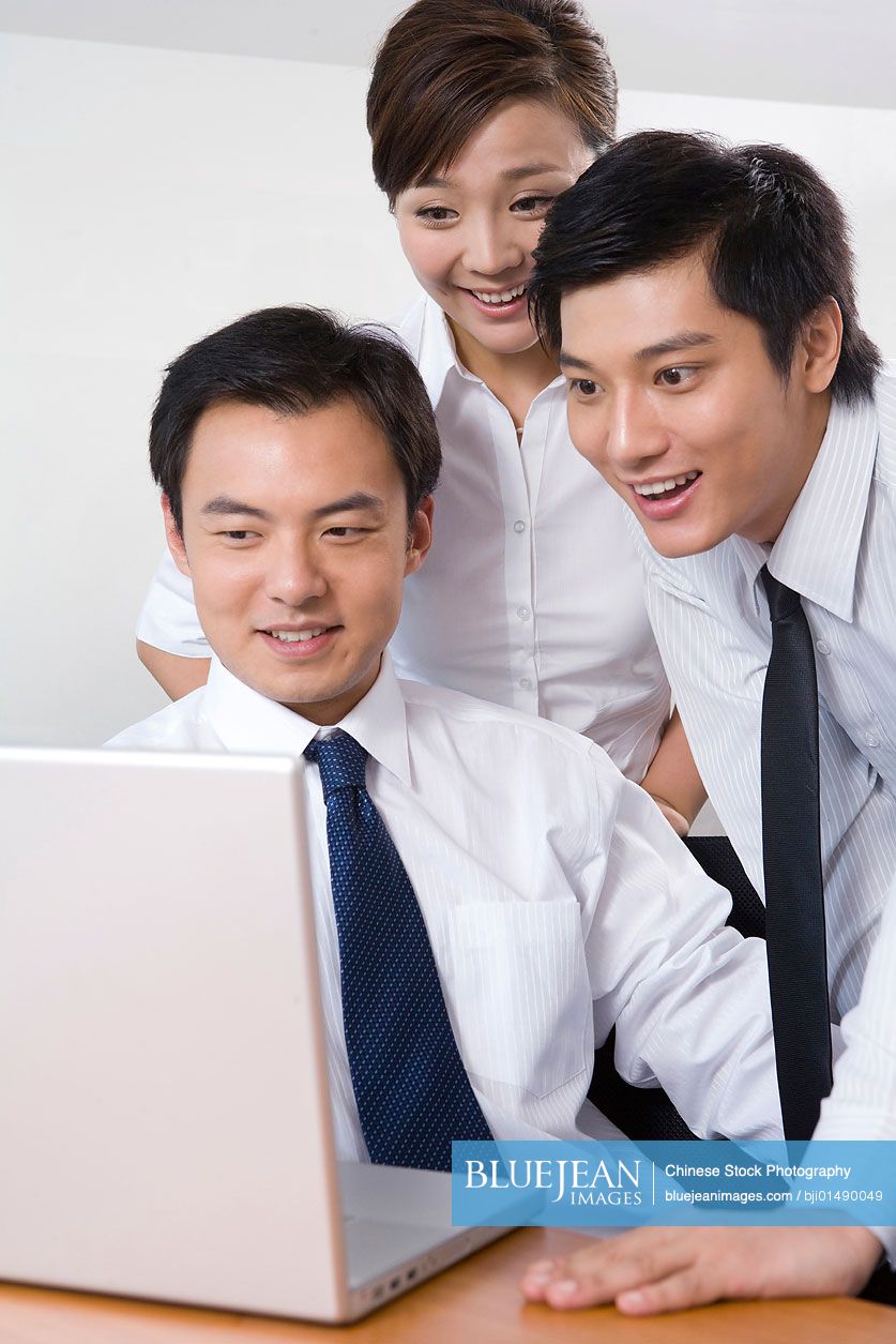 Young Chinese businessmen and businesswoman using laptop in office