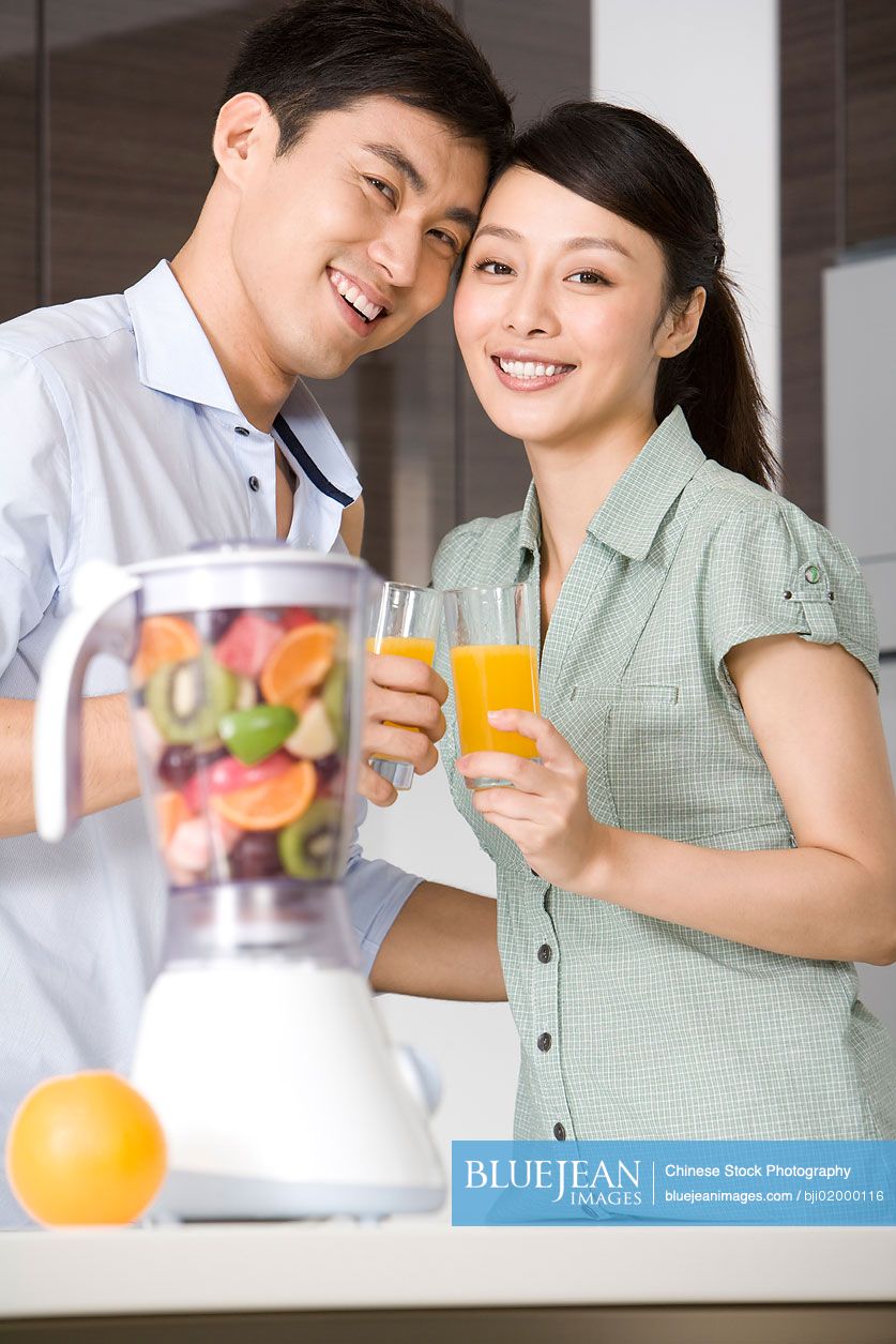 Young Chinese couple drinking fresh fruit juice in kitchen