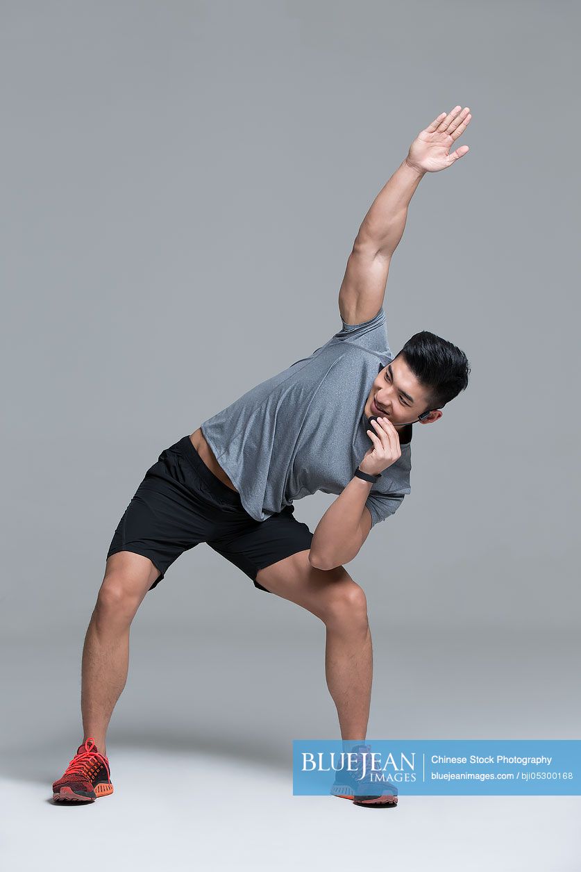 Cheerful young Chinese male trainer with headset teaching at gym