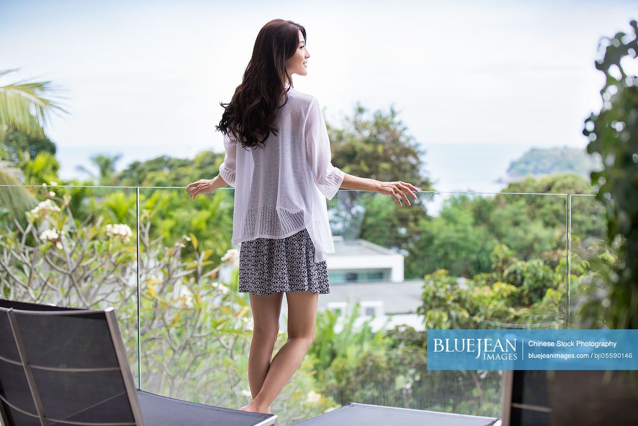 Happy young Chinese woman relaxing on balcony