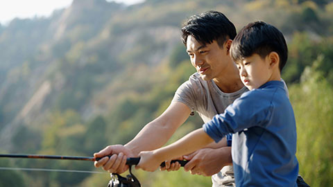 Cheerful Chinese father teaching son fishing