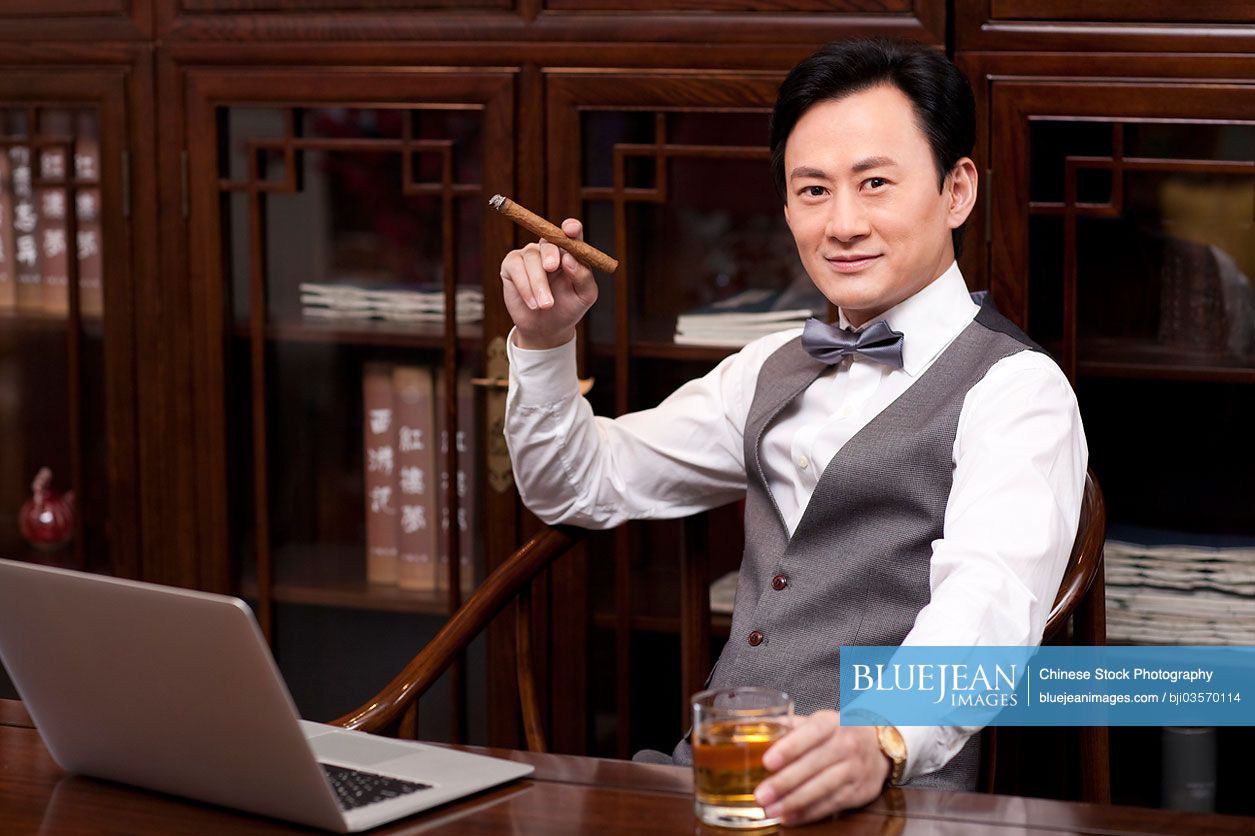 Successful Chinese businessman with cigar and drink in hands