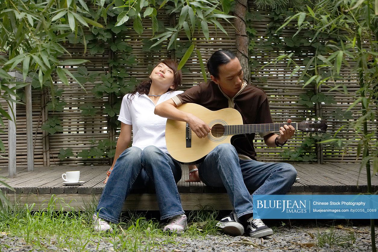 Young Chinese man playing guitar while young woman listens and smiles