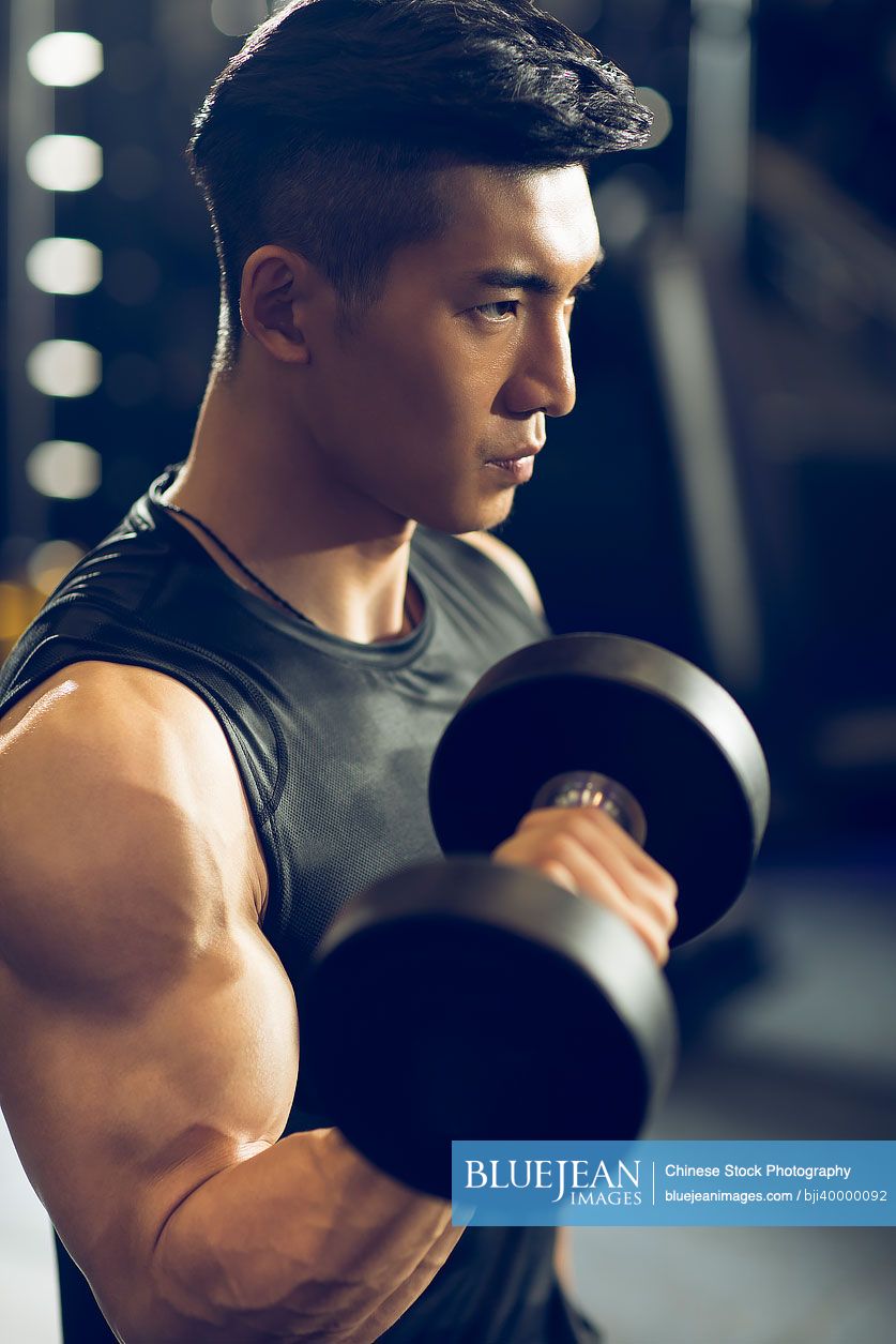 Young Chinese man working out with dumbbell at gym