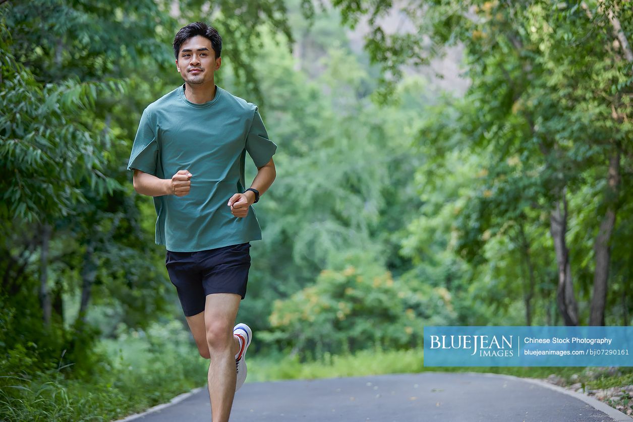 Man jogging along a road surrounded by lush trees