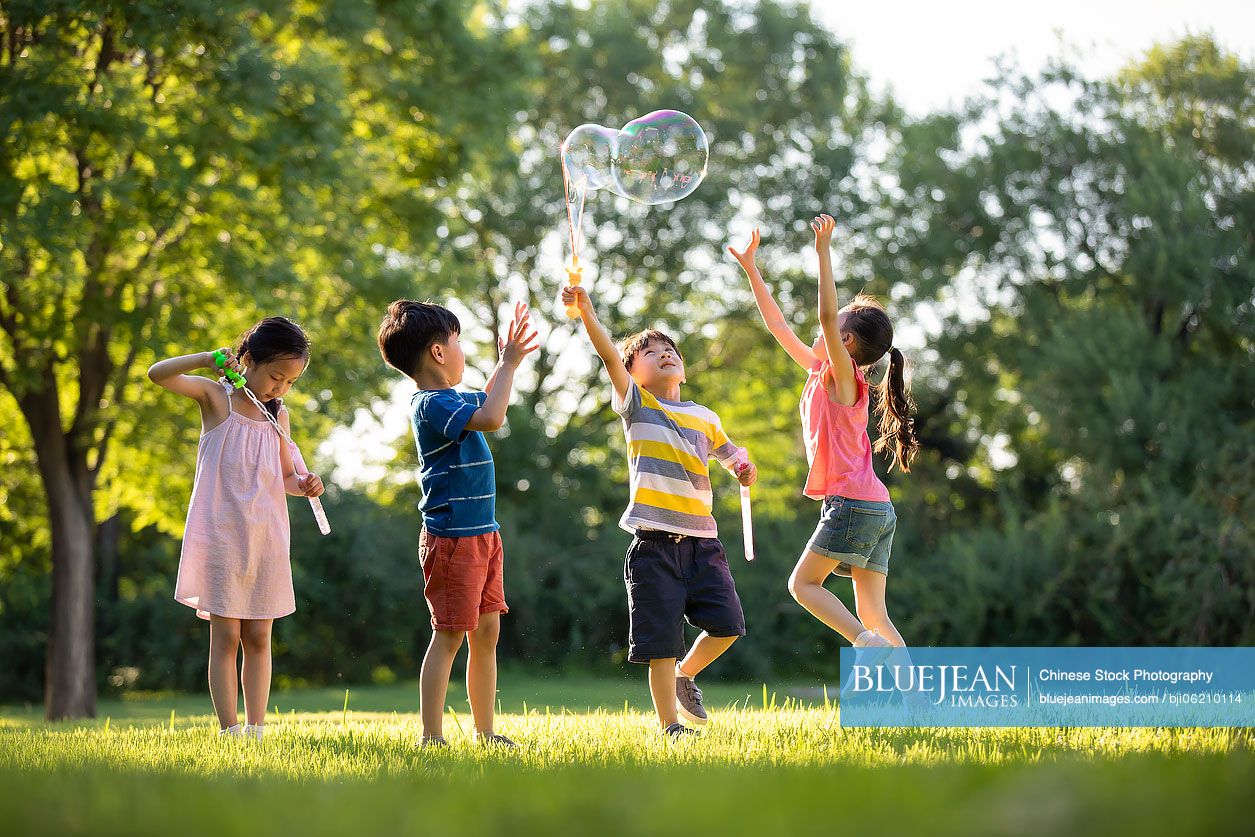 Happy Chinese children blowing bubbles on meadow