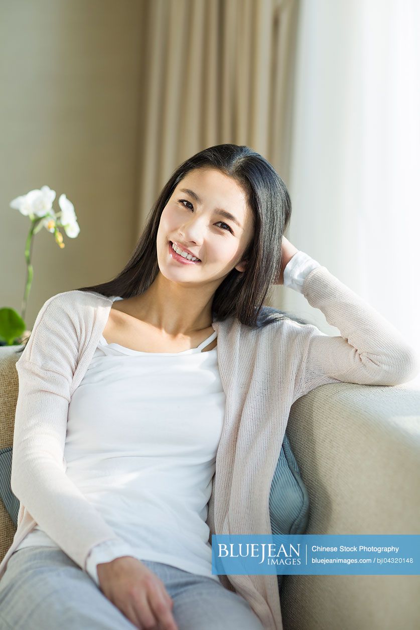 Happy young Chinese woman sitting on sofa