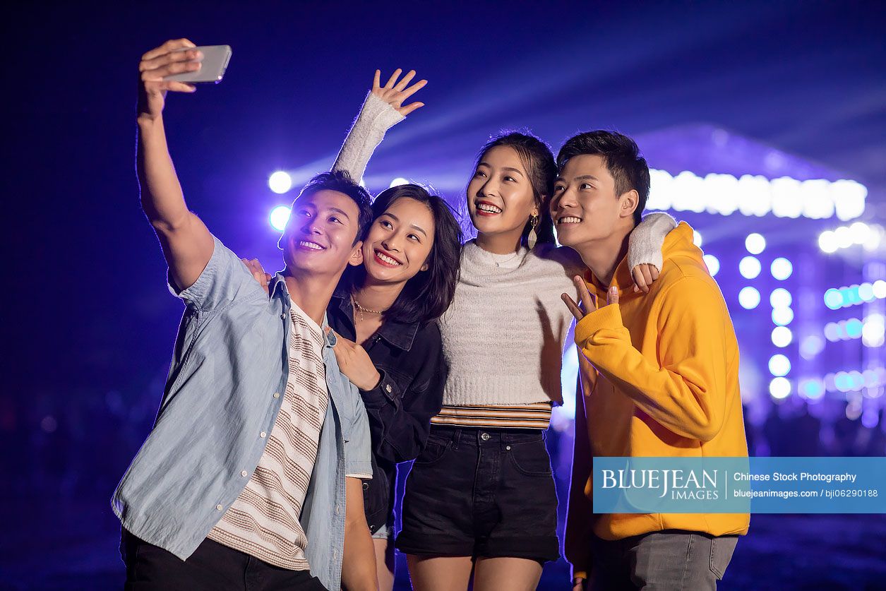Happy young Chinese friends taking selfie at music festival